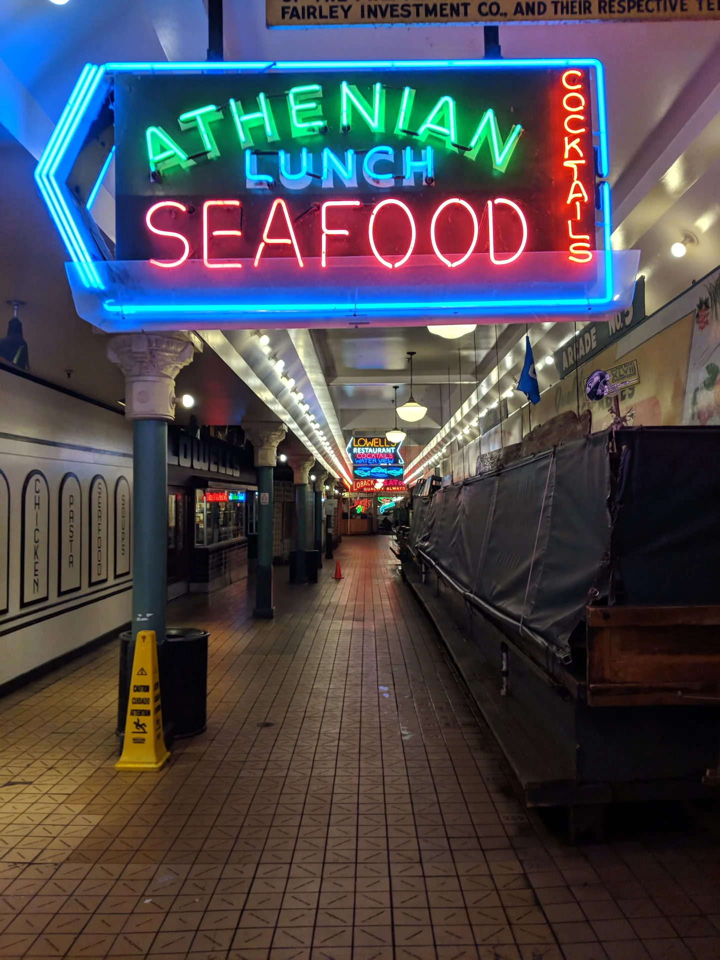 Pike Place Market corridor at night, empty and closed, Athenian Seafood neon sign glowing blue and red, wet tile floor stretching into the distance