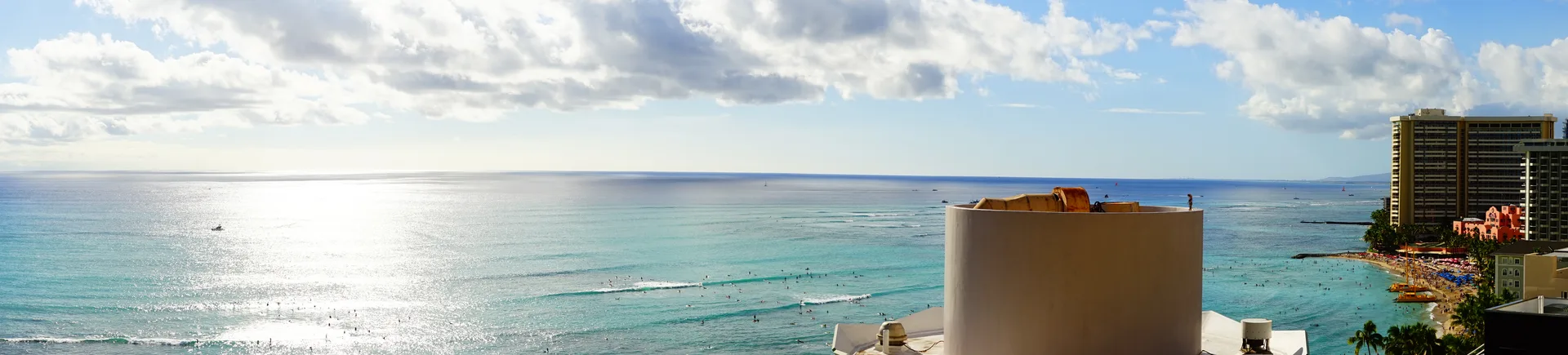 Panoramic view from a high hotel floor overlooking Waikiki beach, silver ocean stretching to the horizon under scattered clouds