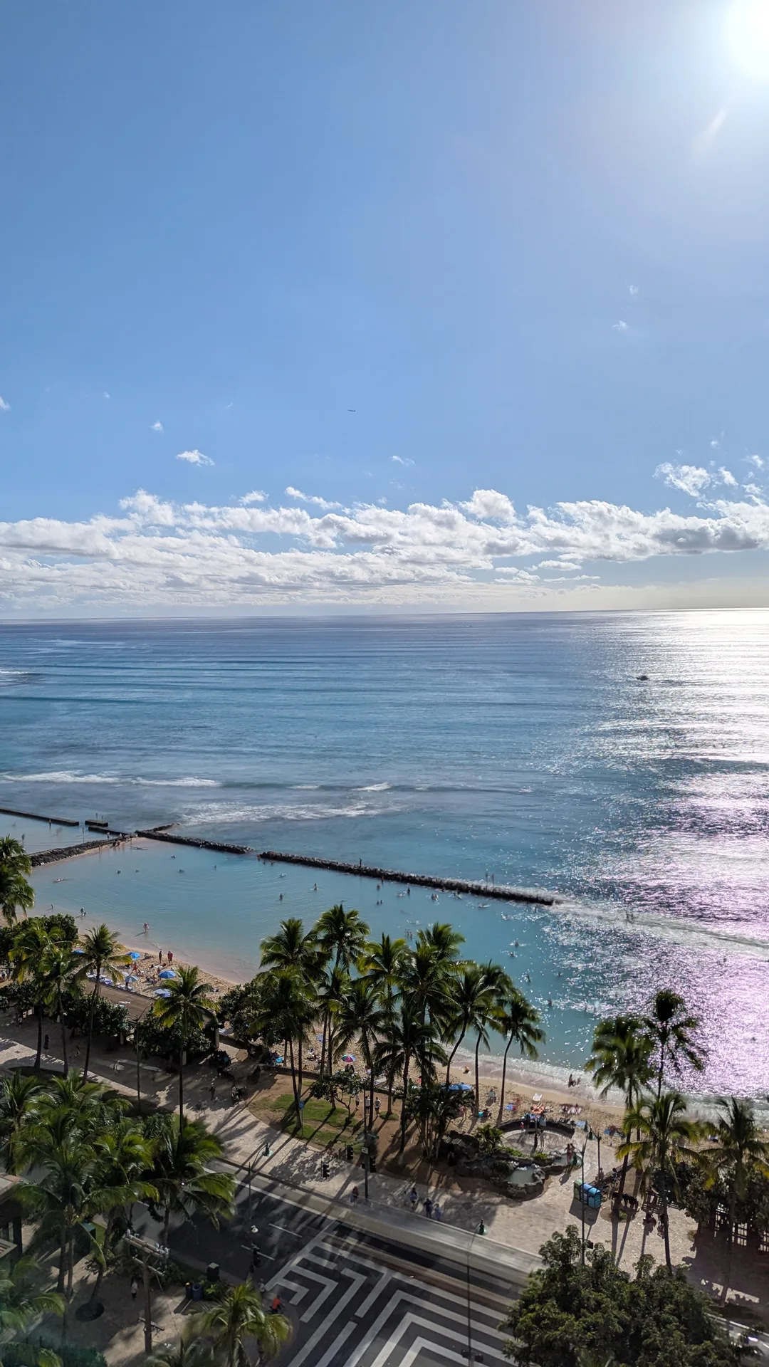 Long exposure shot looking down at Waikiki from above, palm trees lining the boulevard, breakwater and calm turquoise water below