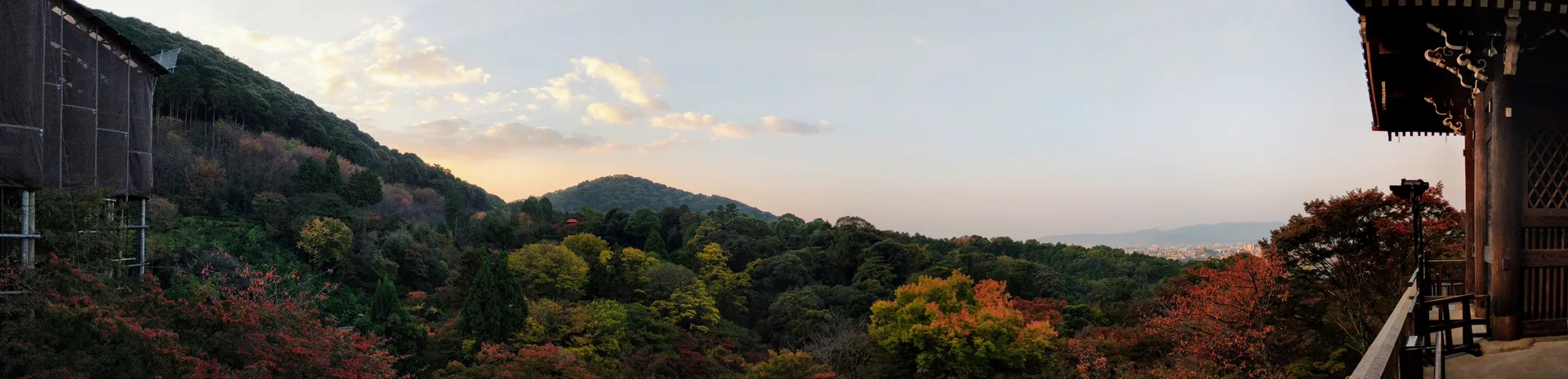Panoramic dawn view from a temple veranda, autumn foliage covering hillsides in mixed greens, oranges, and reds, mountains fading into haze